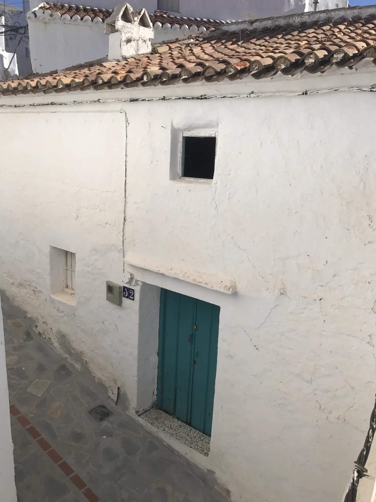 Fachada encalada de una casa de dos plantas con puerta de madera verde y tejado de teja árabe en una calle estrecha de pueblo